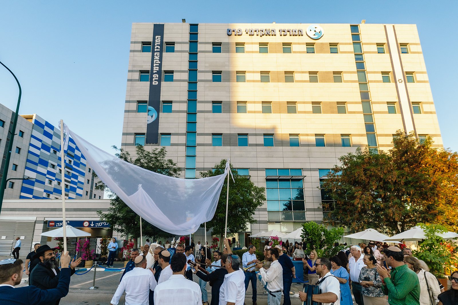 A crowd gathered under a canopy outside the Peres Academic Center building